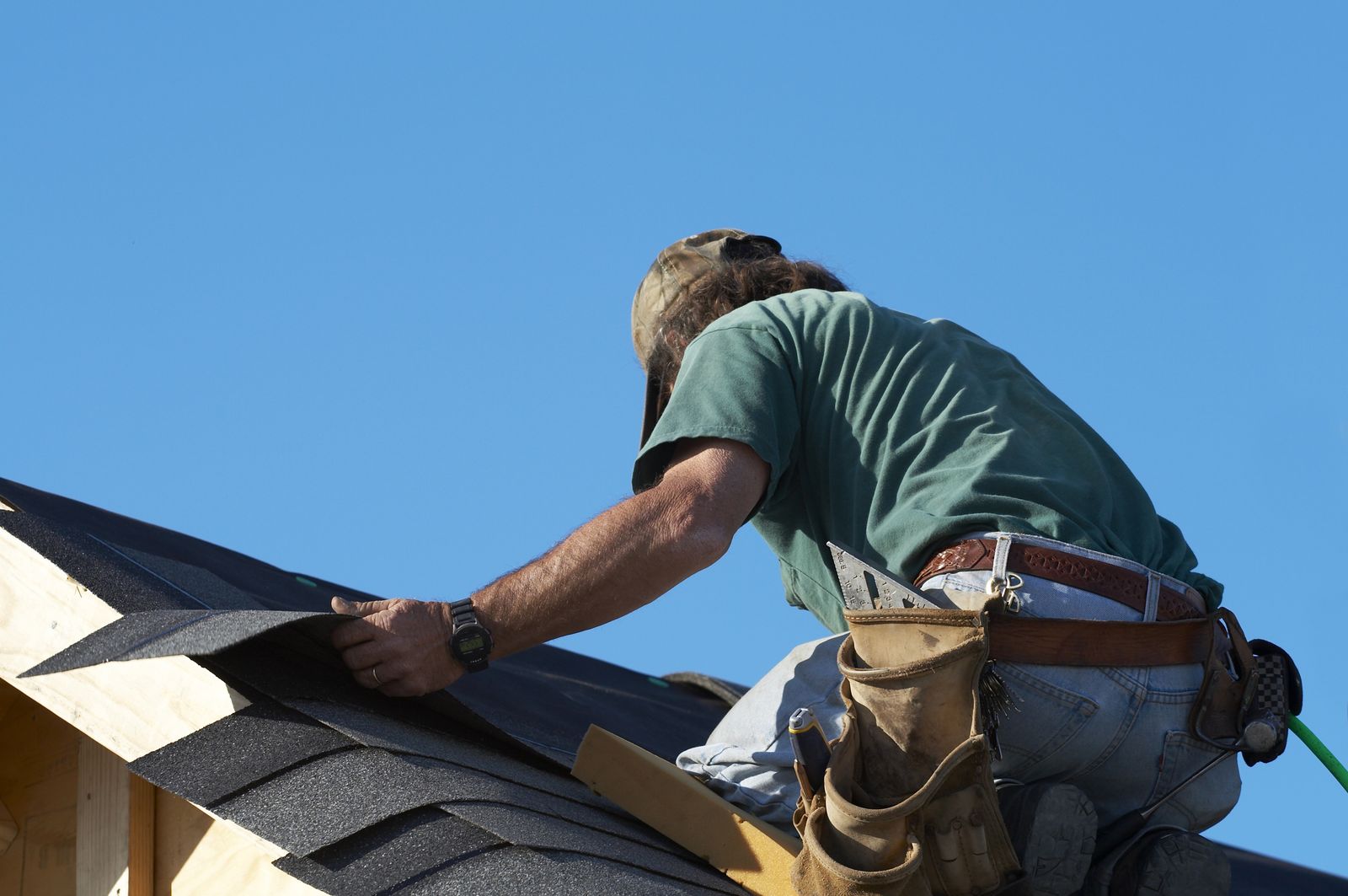 Roofer setting the first course of shingles on a ridge under a clear sky