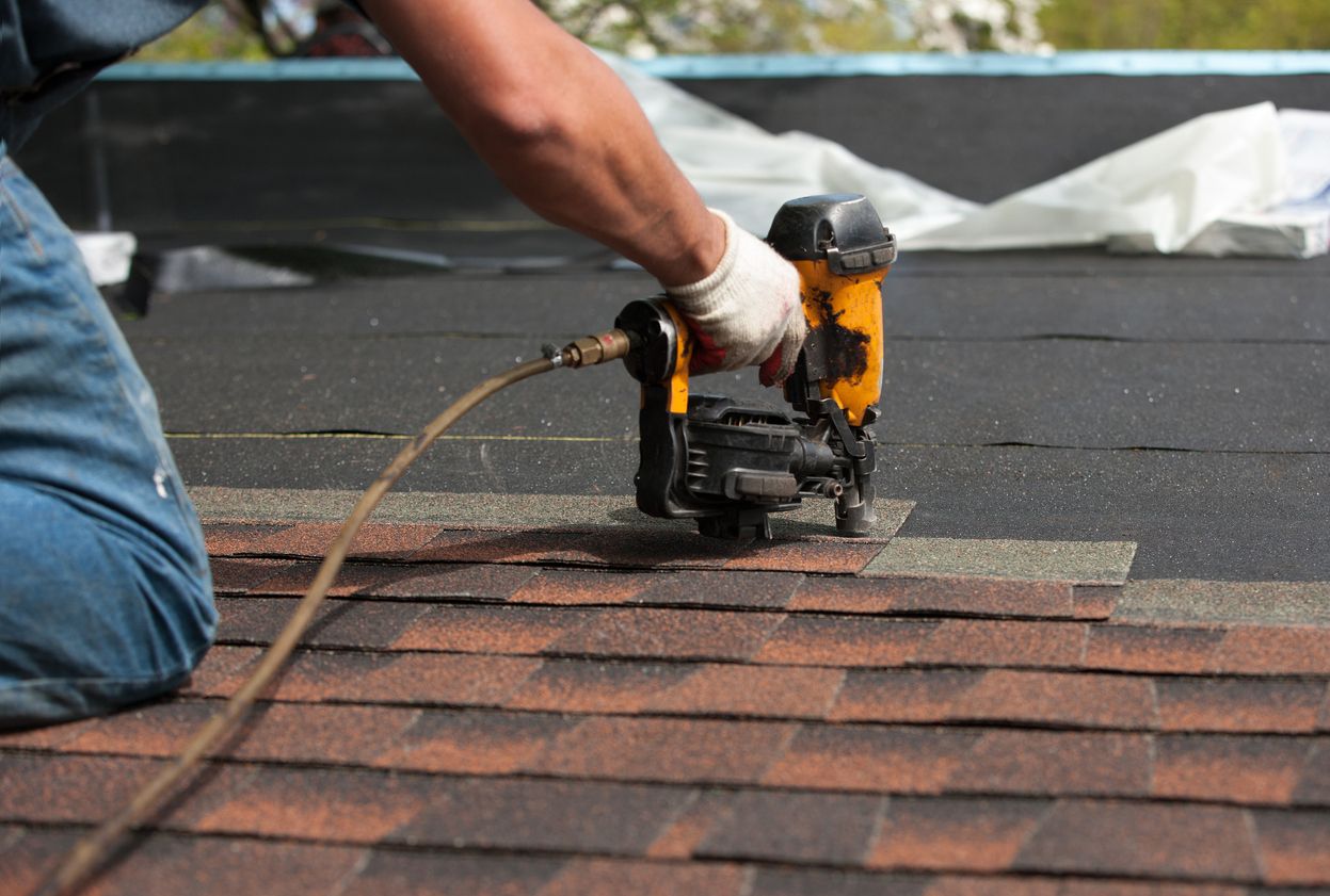 Roofer nailing a shingle course with a pneumatic nail gun